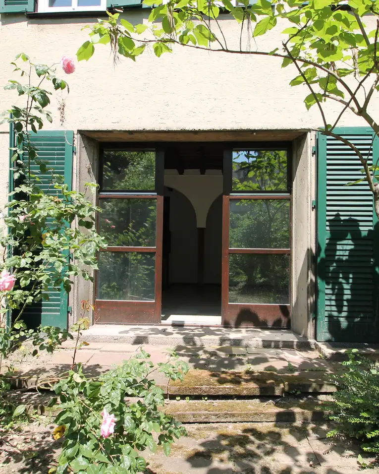 Gartenzugang mit Rosen und grünen Fensterläden