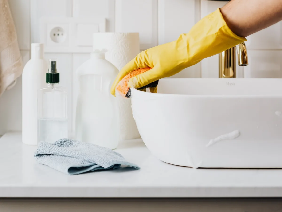 Waschbecken wird mit Schwamm und Handschuh gereinigt