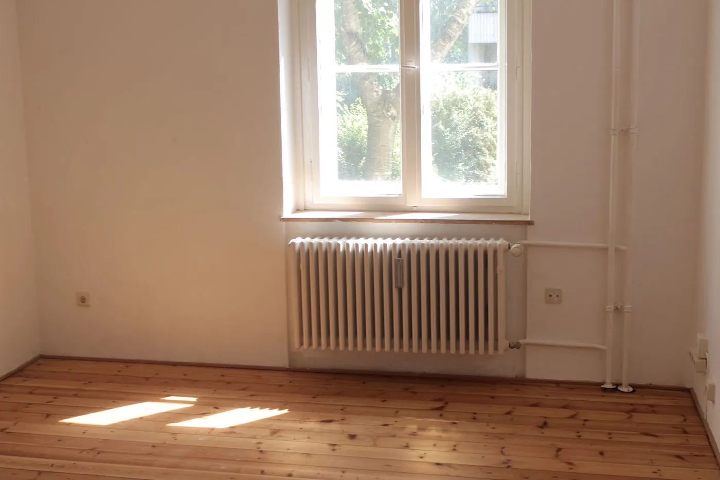 Leeres Zimmer mit Holzdielen, Heizkörper und Sprossenfenster