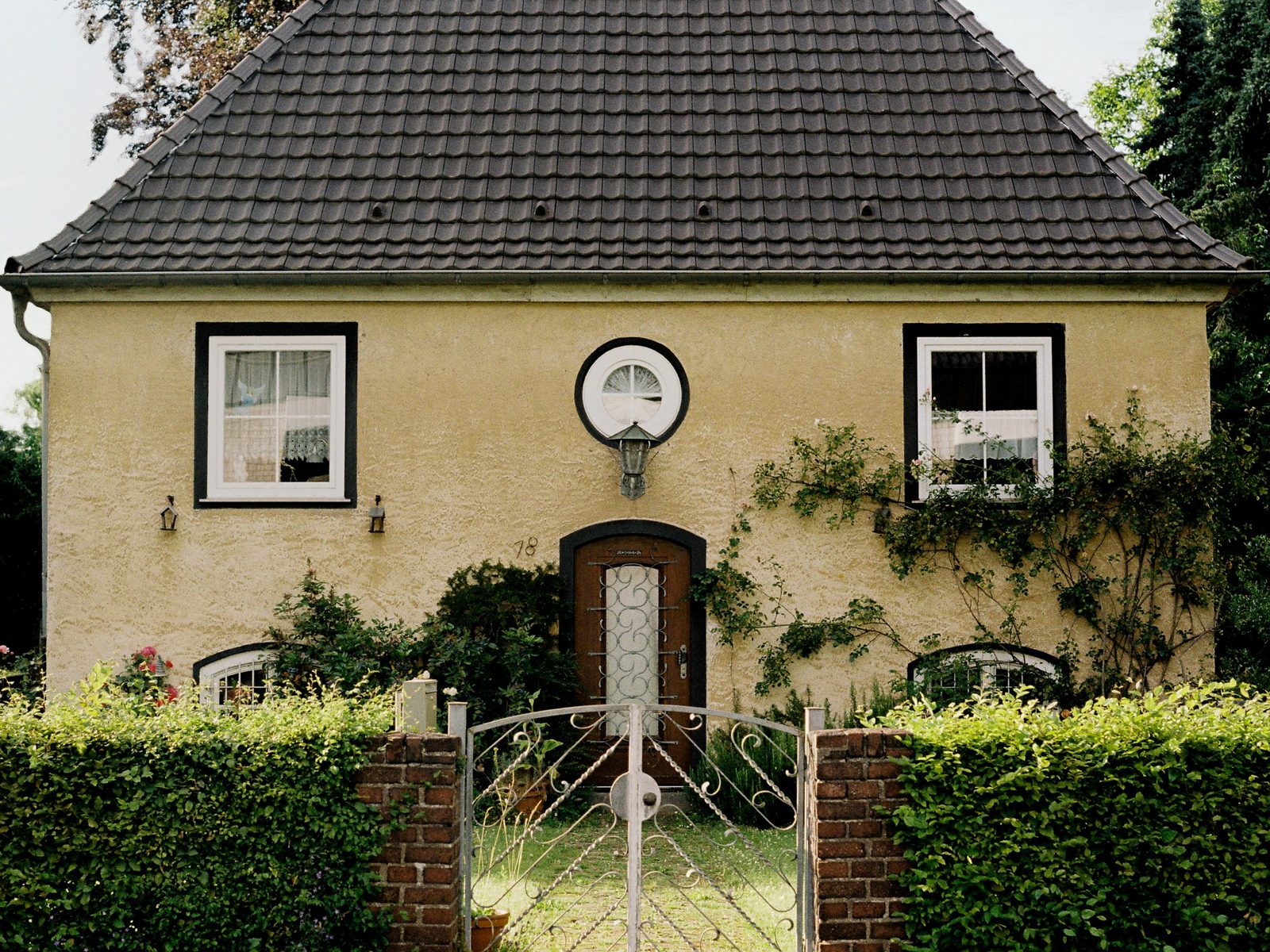 Gelbes Einfamilienhaus mit Hecke und Gartentor