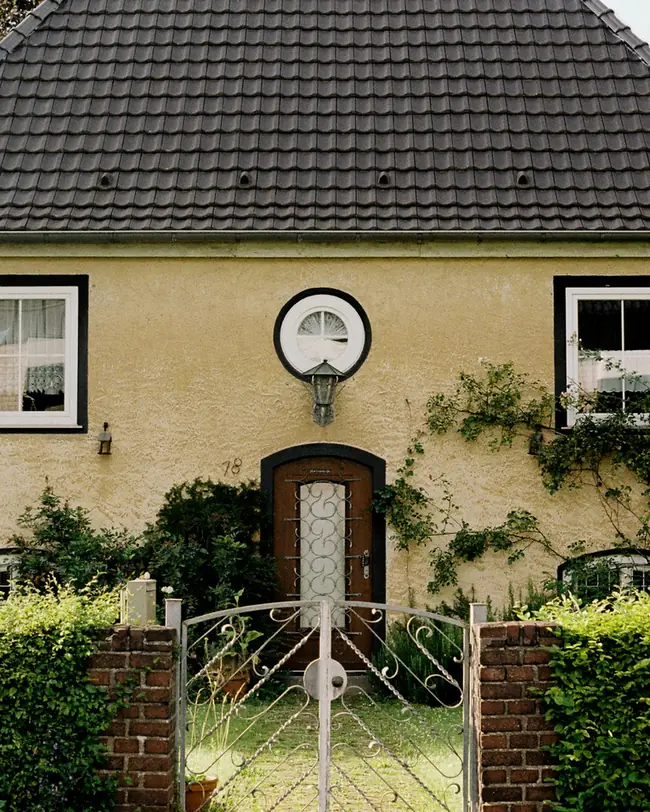 Gelbes Einfamilienhaus mit Hecke und Gartentor